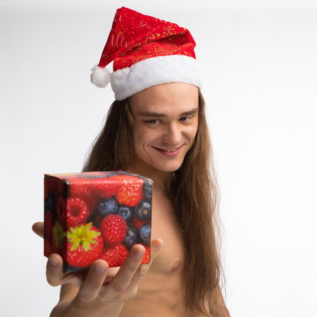 athlete bodybuilder shirtless with long hair posing in cap Santa Claus with a gift in hand on white backgroundの写真素材