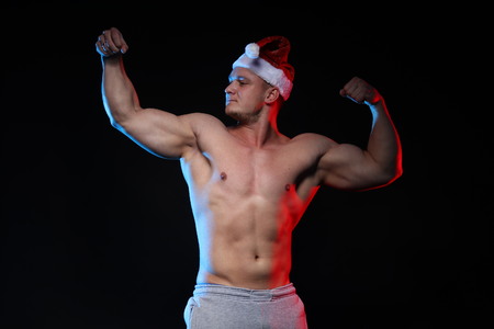 portrait of an athlete bodybuilder posing in cap Santa Claus on a black backgroundの写真素材