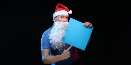 portrait actor male in cap and beard of Santa Claus with a sheet of paper for notes in the hands on a black backgroundの写真素材