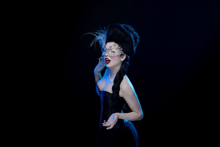 brunette woman with high hair, a mask with feathers and corset in old style on a black backgroundの写真素材