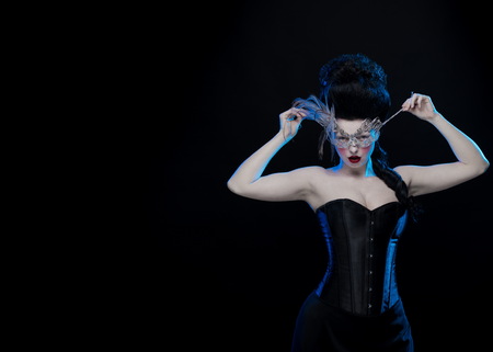 brunette woman with high hair, a mask with feathers and corset in old style on a black backgroundの写真素材