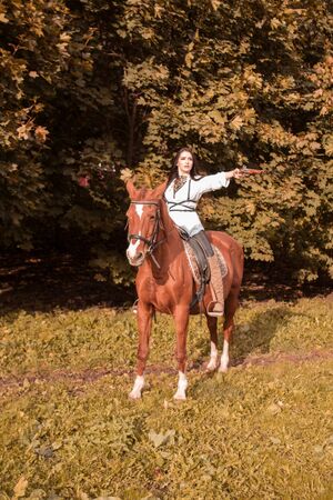 Young brunette woman with long hair posing with a brown red horse in a forest in a sunny meadow