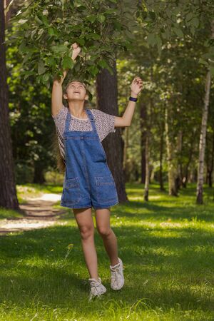 Emotional teenager girl with long hair in blue denim shorts walks in the park on a sunny day.の写真素材