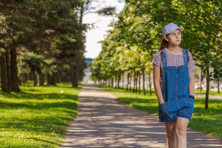 Emotional teenager girl with long hair in blue denim shorts walks in the park on a sunny day.の写真素材