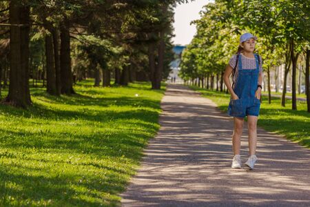 Emotional teenager girl with long hair in blue denim shorts walks in the park on a sunny day.の写真素材