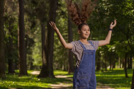 Emotional teenager girl with long hair in blue denim shorts walks in the park on a sunny day.の写真素材