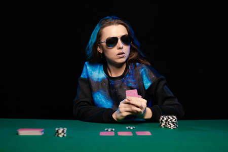 woman in blue clothes and sunglasses is playing cards in a casino on green cloth on a table