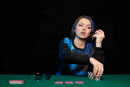 woman in blue clothes and sunglasses is playing cards in a casino on green cloth on a tableの写真素材