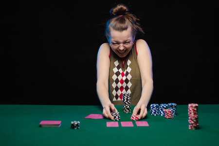 Emotional young girl with glasses playing cards on a table on green cloth at a casinoの写真素材