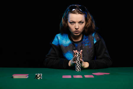 woman in blue clothes and sunglasses is playing cards in a casino on green cloth on a tableの写真素材