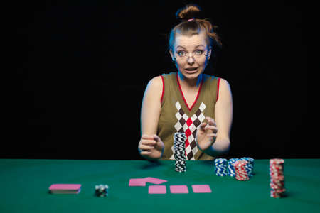 Emotional young girl with glasses playing cards on a table on green cloth at a casino