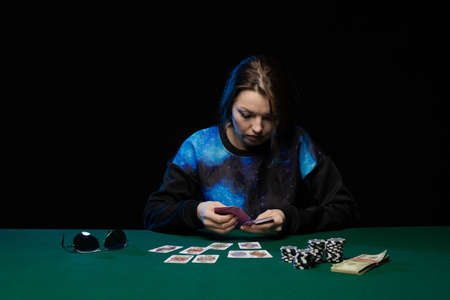 woman in blue clothes and sunglasses is playing cards in a casino on green cloth on a tableの写真素材