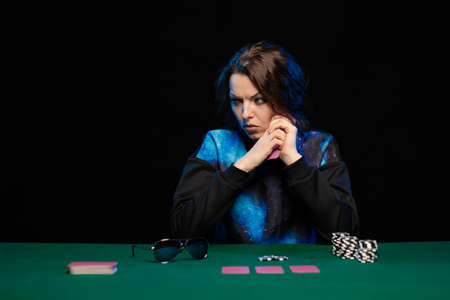 woman in blue clothes and sunglasses is playing cards in a casino on green cloth on a tableの写真素材