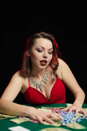 Emotional woman in an evening red dress playing cards with money on the table on a green cloth in a casinoの写真素材