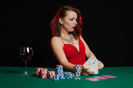 Emotional woman in an evening red dress playing cards with money on the table on a green cloth in a casinoの写真素材