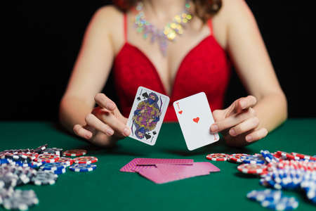 Emotional young girl in an evening red dress playing cards with money on the table on a green cloth...
