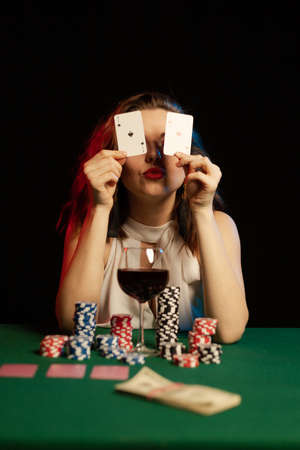 Emotional young woman playing cards with money on a table on green cloth in a casino