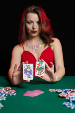 Emotional young lady in an evening red dress playing cards on a table on green cloth in a casinoの写真素材