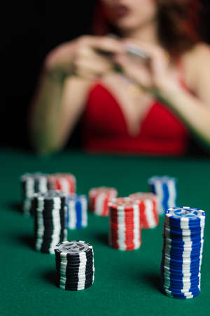 Emotional young lady in an evening red dress playing cards on a table on green cloth in a casinoの写真素材