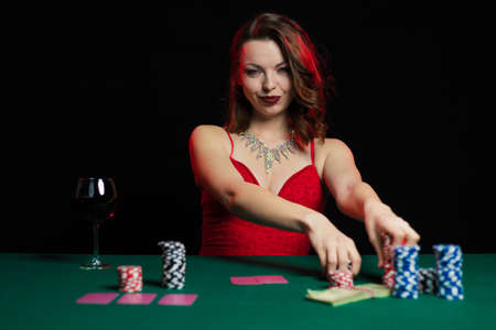 Emotional young lady in an evening red dress playing cards on a table on green cloth in a casinoの写真素材