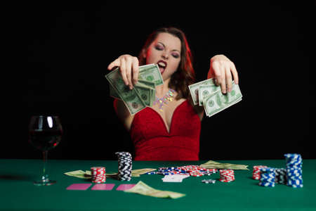 Emotional young lady in an evening red dress playing cards on a table on green cloth in a casino