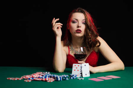 Emotional young woman in an evening red dress playing cards with money on the table on a green cloth in a casinoの写真素材