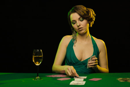 A young lady in a green dress playing cards on a table on a green cloth in a casino