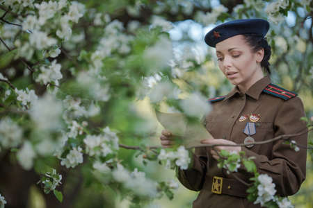 A young female pilot in uniform of Soviet Army pilots during the World War II. Military shirt and a beret. In spring blooming apple orchardの写真素材