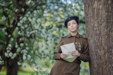 A young female pilot in uniform of Soviet Army pilots during the World War II. Military shirt and a beret. In spring blooming apple orchardの写真素材