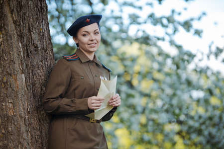 A young female pilot in uniform of Soviet Army pilots during the World War II. Military shirt and a beret. In spring blooming apple orchardの写真素材