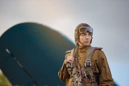 A young female pilot in uniform of Soviet Army pilots during the World War II. Military shirt with shoulder straps of a major, parachute, flight helmet and goggles.の写真素材