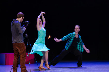 A pair of dancers a man and a woman are dancing on stage and a man videographer records a video clip...