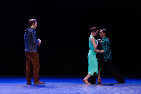 A pair of dancers a man and a woman are dancing on stage and a man videographer records a video clip...