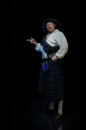Emotional Man with a beard in a blue checkered Scottish costume posing on a black background