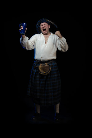 Emotional Man with a beard in a blue checkered Scottish costume posing on a black background