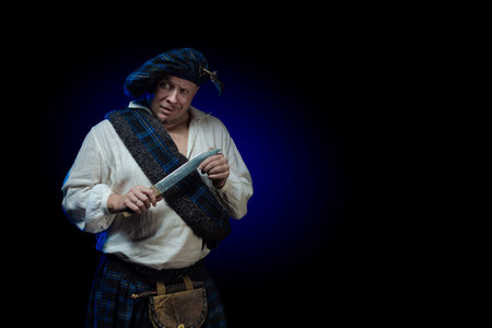 Emotional Man with a beard in a blue checkered Scottish costume posing on a black background