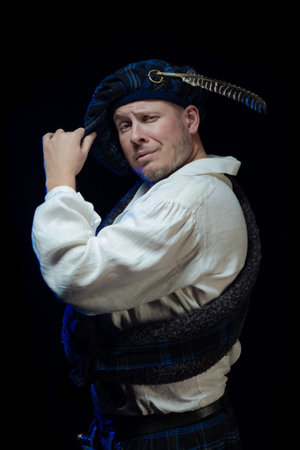 Emotional Man with a beard in a blue checkered Scottish costume posing on a black background