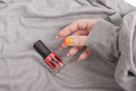 Female hand with long nails and yellow, orange and red gradient manicure and a bottle of nail polish