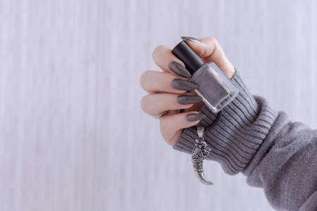 Female hand with long nails and gray black manicure with bottles of nail polishの写真素材