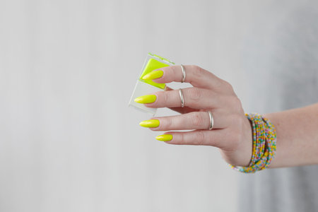 Female hand with long nails and a bottle of bright neon yellow green nail polish