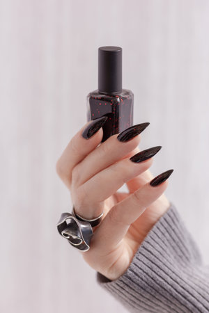 Female hand with long nails and gray black manicure with bottles of nail polish