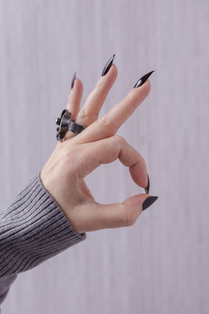 Female hand with long nails and gray black manicure with bottles of nail polish