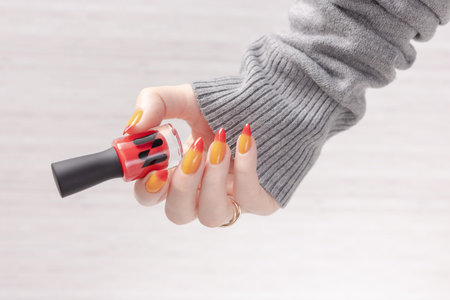 Female hand with long nails and yellow, orange and red gradient manicure holds a bottle of nail polishの写真素材