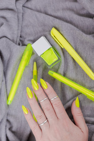 Female hand with long nails and a bottle of bright neon yellow green nail polish