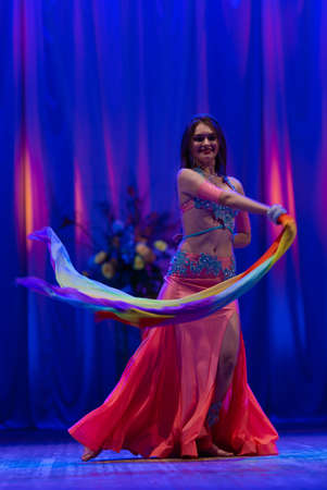 Dancer with long hair in orange neon oriental costumes dance belly dance on the concert stageの写真素材