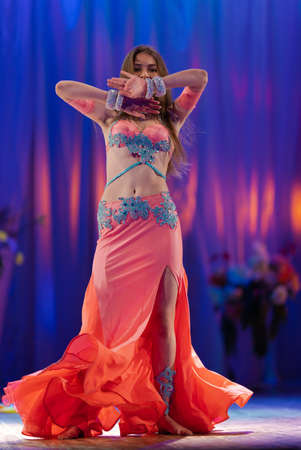Dancer with long hair in orange neon oriental costumes dance belly dance on the concert stageの写真素材
