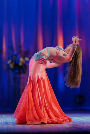 Dancer with long hair in orange neon oriental costumes dance belly dance on the concert stageの写真素材