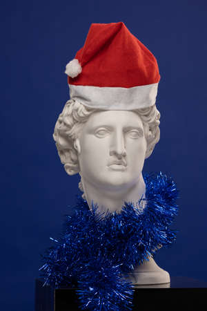 White plaster Statue of Apollo Belvedere in a red cap of Santa Claus and with blue tinselの写真素材