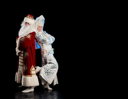 Santa Claus in a red suit and the Snow Maiden in a white fur coat posing against a black backgroundの写真素材
