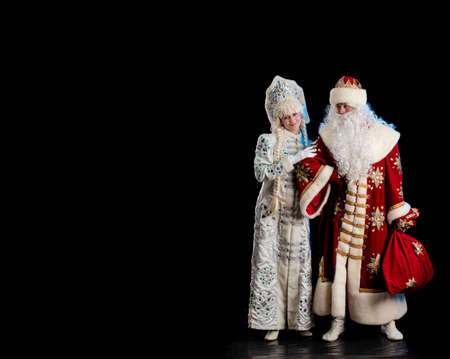 Santa Claus in a red suit and the Snow Maiden in a white fur coat posing against a black backgroundの写真素材